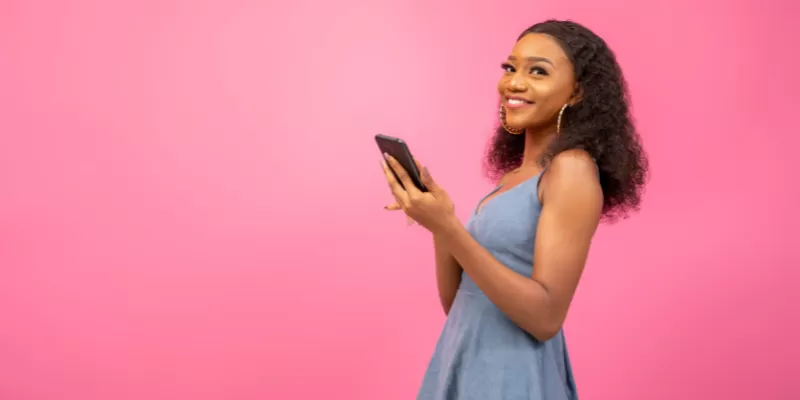 smiling african american woman holding mobile phone on a pink background